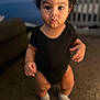 Terry is registered to the contest to win money with this photo: toddler, child, baby, onesie, black_clothing, socks, indoor, carpet, walking, person, curly_hair, face, expression, young_child, home, blurred_background, standing, cute, small_hands, big_eyes