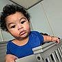 Terry is registered to the contest to win money with this photo: toddler, child, baby, crib, blue_shirt, curly_hair, indoors, furniture, hand, face, expression, person, young_child, skin, room, wall, portrait, looking, standing, casual
