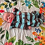 baby, infant, striped_clothing, lying_down, blanket, floral_pattern, cartoon_animals, giraffe, elephant, lion, blue, brown, pink, green, yellow, face, person, cute, child, indoors