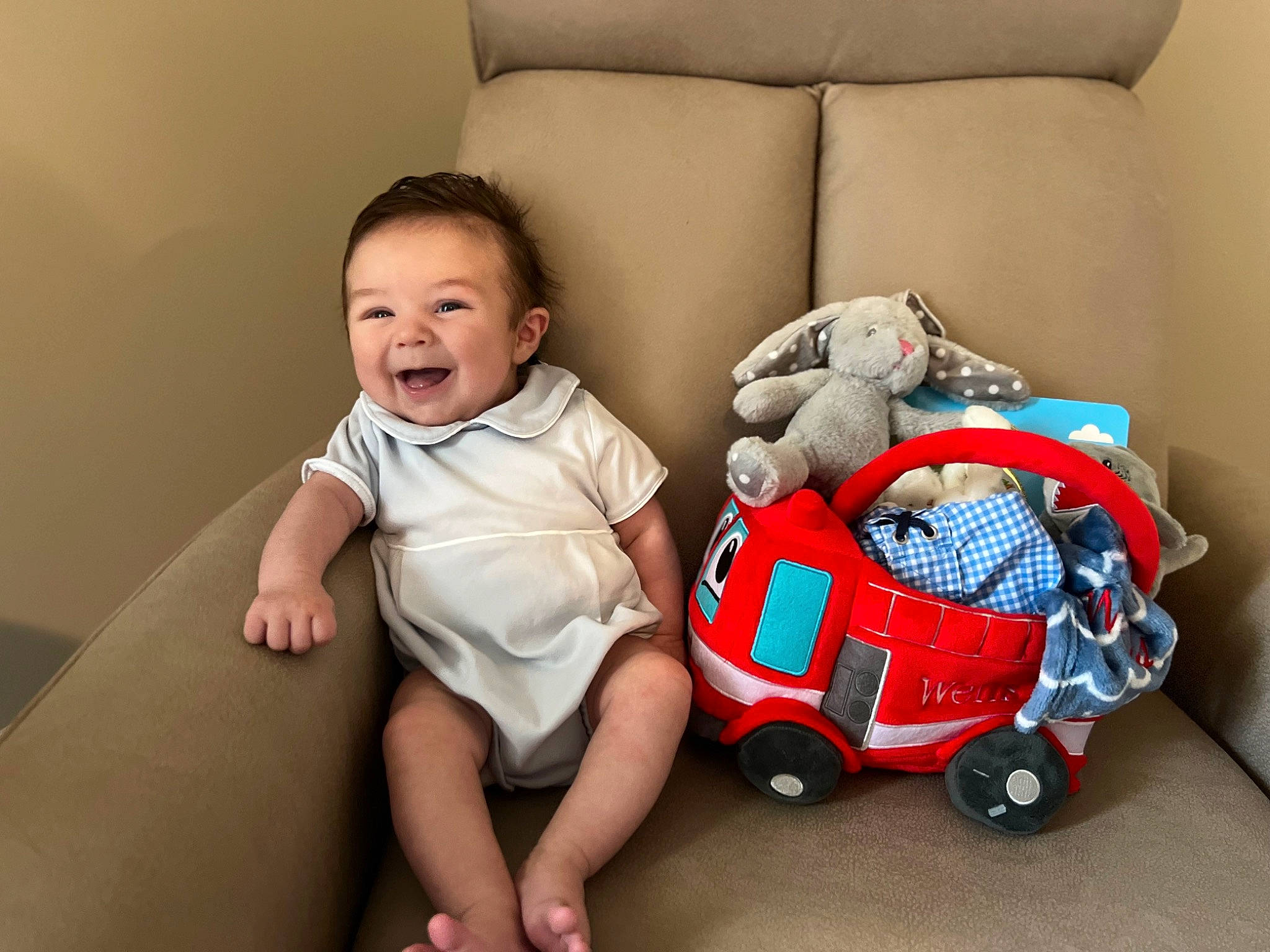 Wells is registered to the contest to win money with this photo: baby, baby_carriage, baby_toddler_clothing, bag, carmine, child, comfort, couch, flash_photography, flooring, happy, human_leg, person, room, shoe, sitting, smile, tire, toddler, vertebrate