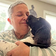 Tosca a rejoint le concours — aidez-le/la à gagner de superbes lots ! person, dog, affection, hug, indoor, smile, pet, love, face, closeup, cozy, light, window, casual_clothing, gray_hair, black_and_white_dog, human_animal_interaction, portrait, warmth, emotion