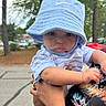 baby, child, hat, blue_hat, striped_shirt, tattoo, arm, outdoor, trees, parking_lot, person, holding, cute, curious, infant, casual_clothing, daytime, nature, portrait, expression