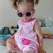 Nysia a rejoint le concours — aidez-le/la à gagner de superbes lots ! toddler, child, sunglasses, pink_romper, pigtails, indoor, table, footwear, casual, baby, cute, fashion, accessory, hair_style, sitting, person, home, relaxed, funny, portrait