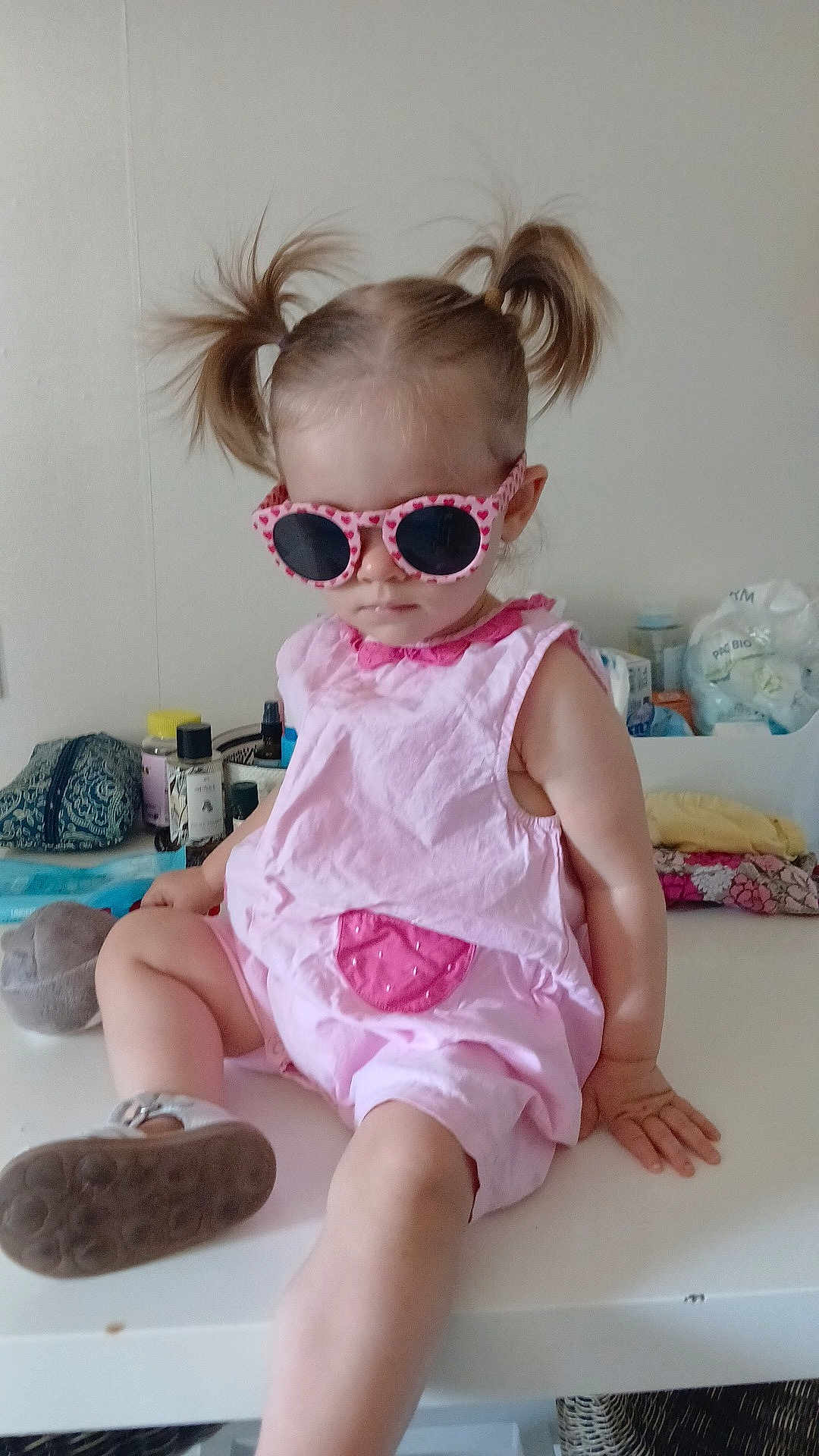 Nysia a rejoint le concours — aidez-le/la à gagner de superbes lots ! toddler, child, sunglasses, pink_romper, pigtails, indoor, table, footwear, casual, baby, cute, fashion, accessory, hair_style, sitting, person, home, relaxed, funny, portrait