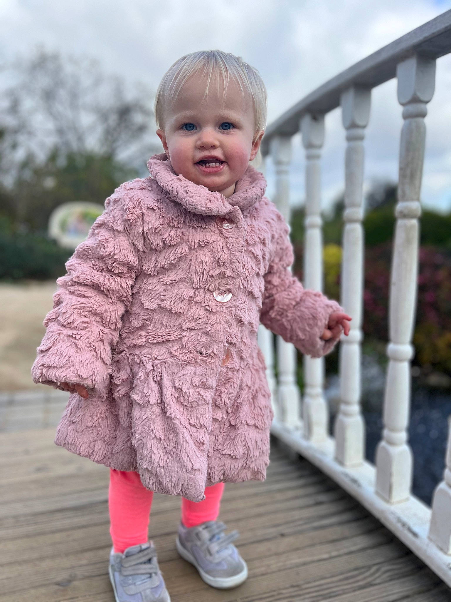 Marina is registered to the contest to win money with this photo: baby, baby_toddler_clothing, child, clothing, cloud, fence, fun, grass, handrail, happy, leg, magenta, pattern, person, pink, sitting, sky, sleeve, smile, standing