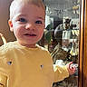 child, toddler, yellow_sweater, smiling, face, person, indoor, glass_cabinet, decor, sunlight, reflection, furniture, hand, blue_eyes, short_hair, cute, happy, young_child, portrait, casual_clothing