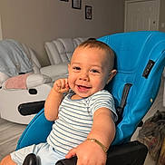 Ayden is registered to the contest to win money with this photo: baby, child, infant, smiling, happy, portrait, indoors, living_room, chair, blue_chair, seated, striped_shirt, light_clothing, short_hair, face, eyes, fist, armrest, furniture, home
