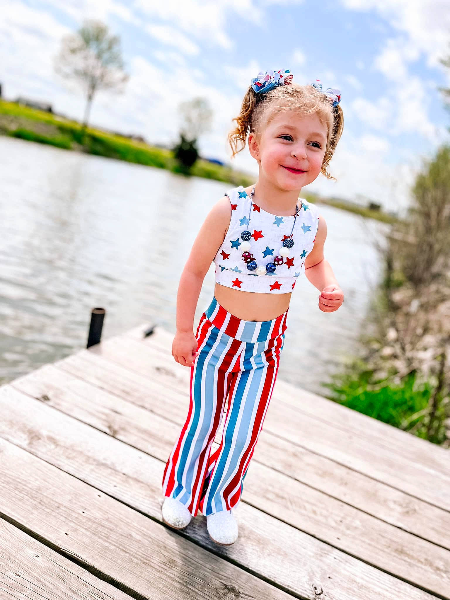 Natalie is registered to the contest to win money with this photo: baby_toddler_clothing, child, clothing, cloud, dress, electric_blue, grass, happy, joy, lake, leisure, people_in_nature, person, plant, sky, smile, standing, street_fashion, toddler, tree