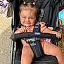 baby, toddler, stroller, child, smile, pigtails, outdoor, toy, clothing, seatbelt, hand, face, blue_eyes, fabric, playful, cute, person, sitting, expression, chicco