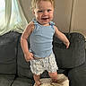 toddler, child, baby, smiling, standing, portrait, indoor, couch, cushion, curly_hair, blue_top, shorts, clothing, curtain, window, home, furniture, happy, playful, photography