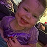 Hadley is registered to the contest to win money with this photo: child, toddler, smiling, portrait, face, indoors, purple_shirt, toy, sitting, close_up, happy, brown_hair, young, person, hand, arm, couch, blanket, warm_lighting, casual_photo