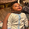 baby, infant, onesie, elephant_pattern, hand, floor, quilt, footwear, indoor, wood_floor, curious, child, person, sitting, casual, blanket, cozy, looking_up, skin, young