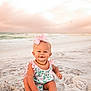 baby, child, beach, sand, ocean, sunset, sky, pink_bow, romper, smiling, sitting, cute, outdoor, nature, water, waves, portrait, happy, infant, summer