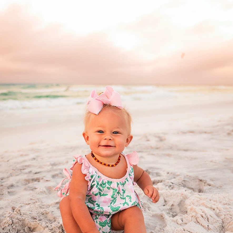 Ellarie is registered to the contest to win money with this photo: baby, beach, child, cute, happy, infant, nature, ocean, outdoor, pink_bow, portrait, romper, sand, sitting, sky, smiling, summer, sunset, water, waves