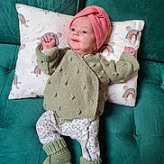 Esmée participe au concours pour gagner de l'argent avec cette photo : baby, infant, couch, pillow, knit_hat, knitted_sweater, booties, green_sofa, rainbow_pattern, floral_pants, lying_down, portrait, face, hands, cozy, textile, home_interior, cute, newborn, smile
