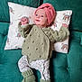 baby, infant, couch, pillow, knit_hat, knitted_sweater, booties, green_sofa, rainbow_pattern, floral_pants, lying_down, portrait, face, hands, cozy, textile, home_interior, cute, newborn, smile