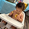 Elijah is registered to the contest to win money with this photo: birthday_party, celebration, child, cupcake, curious, curly_hair, food, frosting, high_chair, indoor, messy, party_decorations, person, plastic_chair, snack_time, socks, table, toddler, wood_floor, young_child