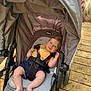 Langston is registered to the contest to win money with this photo: baby, stroller, child, infant, outdoor, wooden_deck, yellow_top, denim_shorts, harness, smiling, blonde_hair, sunlight, shadow, person, seat, canopy, casual_clothing, relaxed, daylight, playful