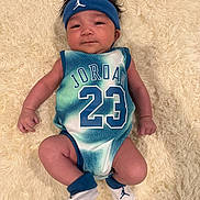 Aspen Julian is registered to the contest to win money with this photo: baby, infant, child, jersey, jordan, number_23, headband, socks, blanket, faux_fur, portrait, lying_down, hands, legs, face, hair, sportswear, blue, white, cute