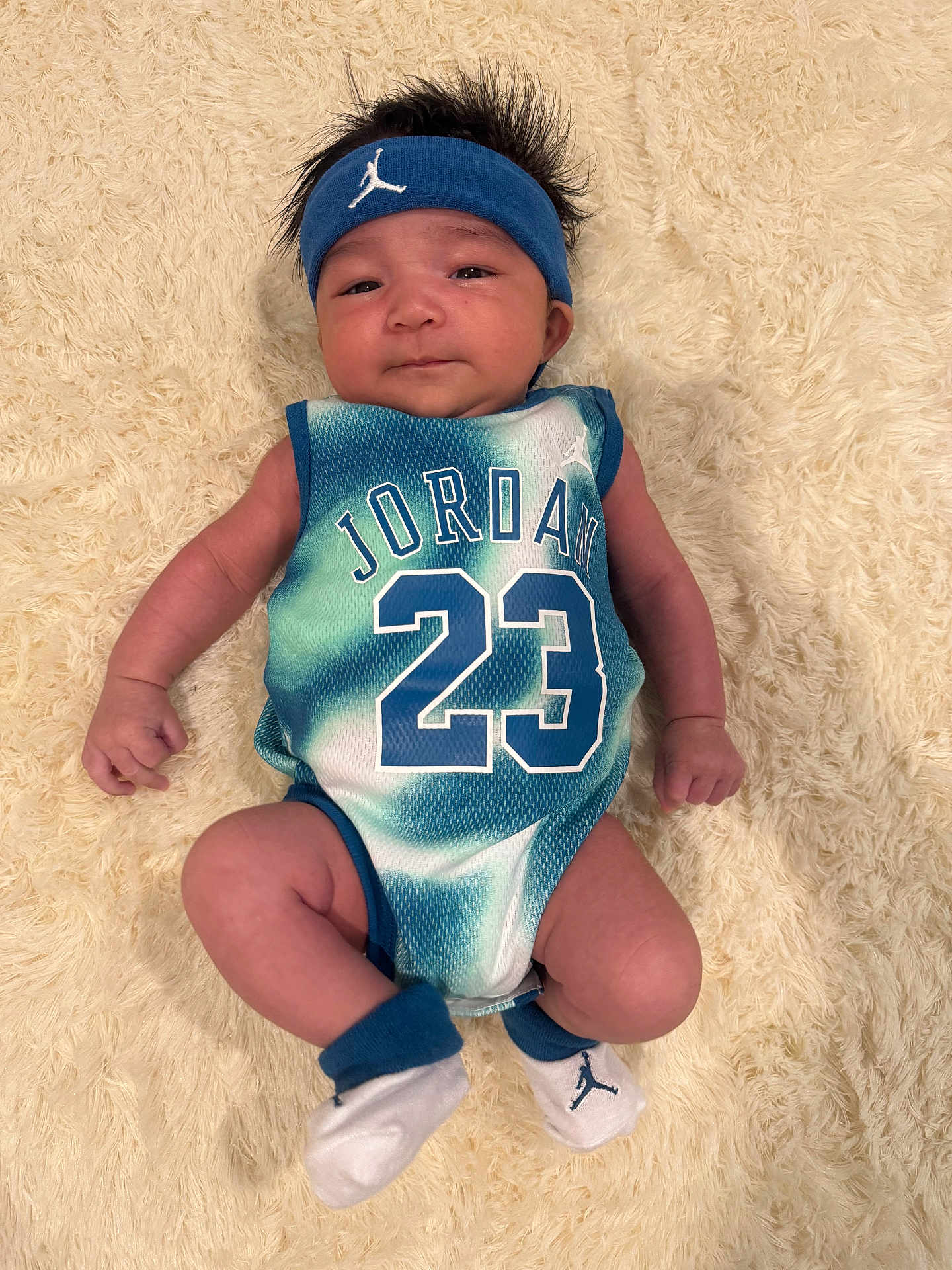 Aspen Julian is registered to the contest to win money with this photo: baby, infant, child, jersey, jordan, number_23, headband, socks, blanket, faux_fur, portrait, lying_down, hands, legs, face, hair, sportswear, blue, white, cute