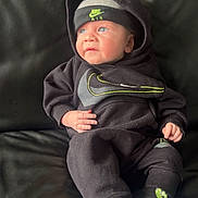 Roman is registered to the contest to win money with this photo: baby, infant, black_clothing, nike, hoodie, hat, socks, couch, leather, blue_eyes, cute, portrait, indoor, child, small_hand, sitting, looking_away, cozy, casual, comfortable