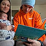 Weston joined the competition — help win amazing prizes! baby, woman, man, family, reading, book, blanket, orange_hoodie, blue_beanie, indoor, living_room, smiling, holding, seated, couch, casual_clothing, portrait, happy, child, parent