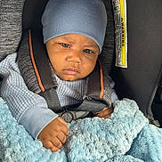 Eyad joined the competition — help win amazing prizes! baby, child, blue_hat, car_seat, blanket, sweater, infant, seatbelt, face, hand, cozy, indoor, person, portrait, cute, clothing, car, safety, warm, expression