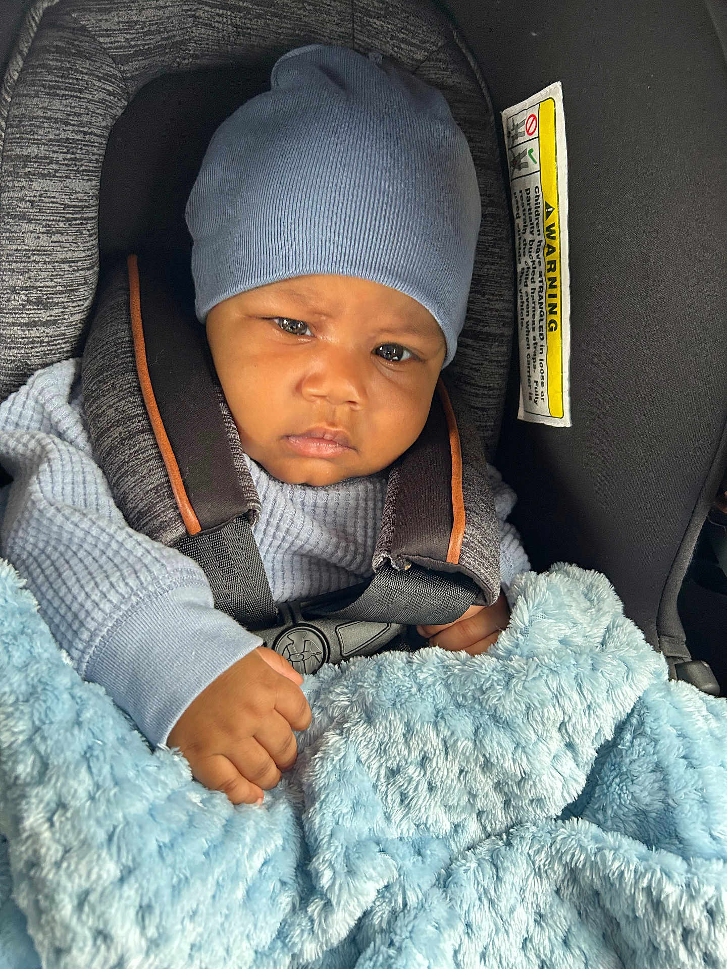 Eyad joined the competition — help win amazing prizes! baby, child, blue_hat, car_seat, blanket, sweater, infant, seatbelt, face, hand, cozy, indoor, person, portrait, cute, clothing, car, safety, warm, expression