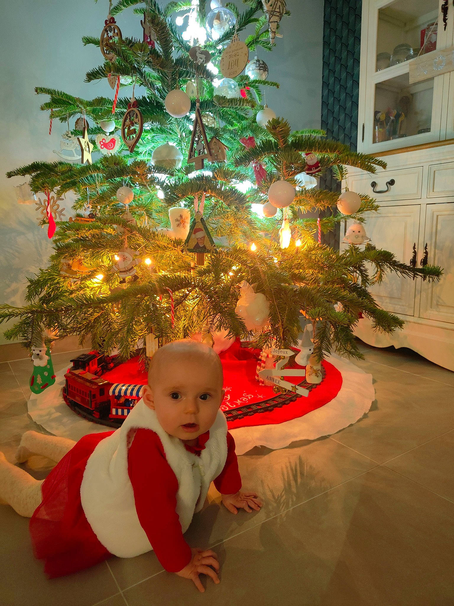 Lou participe au concours pour gagner de l'argent avec cette photo : baby_toddler_clothing, christmas, christmas_decoration, christmas_eve, christmas_ornament, christmas_tree, conifer, event, evergreen, flooring, happy, holiday, holiday_ornament, ornament, person, plant, red, toddler, tree, winter