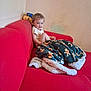 Noé participe au concours pour gagner de l'argent avec cette photo : toddler, child, blanket, red_couch, toy_car, curly_hair, smiling, indoor, wall, sitting, cozy, plush_blanket, gingerbread_pattern, person, home, furniture, playful, cute, young_child, relaxed