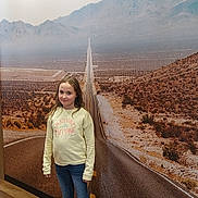 Emie a rejoint le concours — aidez-le/la à gagner de superbes lots ! child, girl, indoor, mural, road, mountains, desert, wall_art, yellow_sweatshirt, jeans, sneakers, flooring, long_road, scenery, portrait, casual_clothing, standing, expression, background, photography