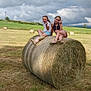 Cléa a rejoint le concours — aidez-le/la à gagner de superbes lots ! child, children, girl, hay_bale, field, grass, outdoor, sky, cloudy_sky, peace_sign, summer, nature, playful, casual_clothing, footwear, rural, farm, greenery, happy, sitting