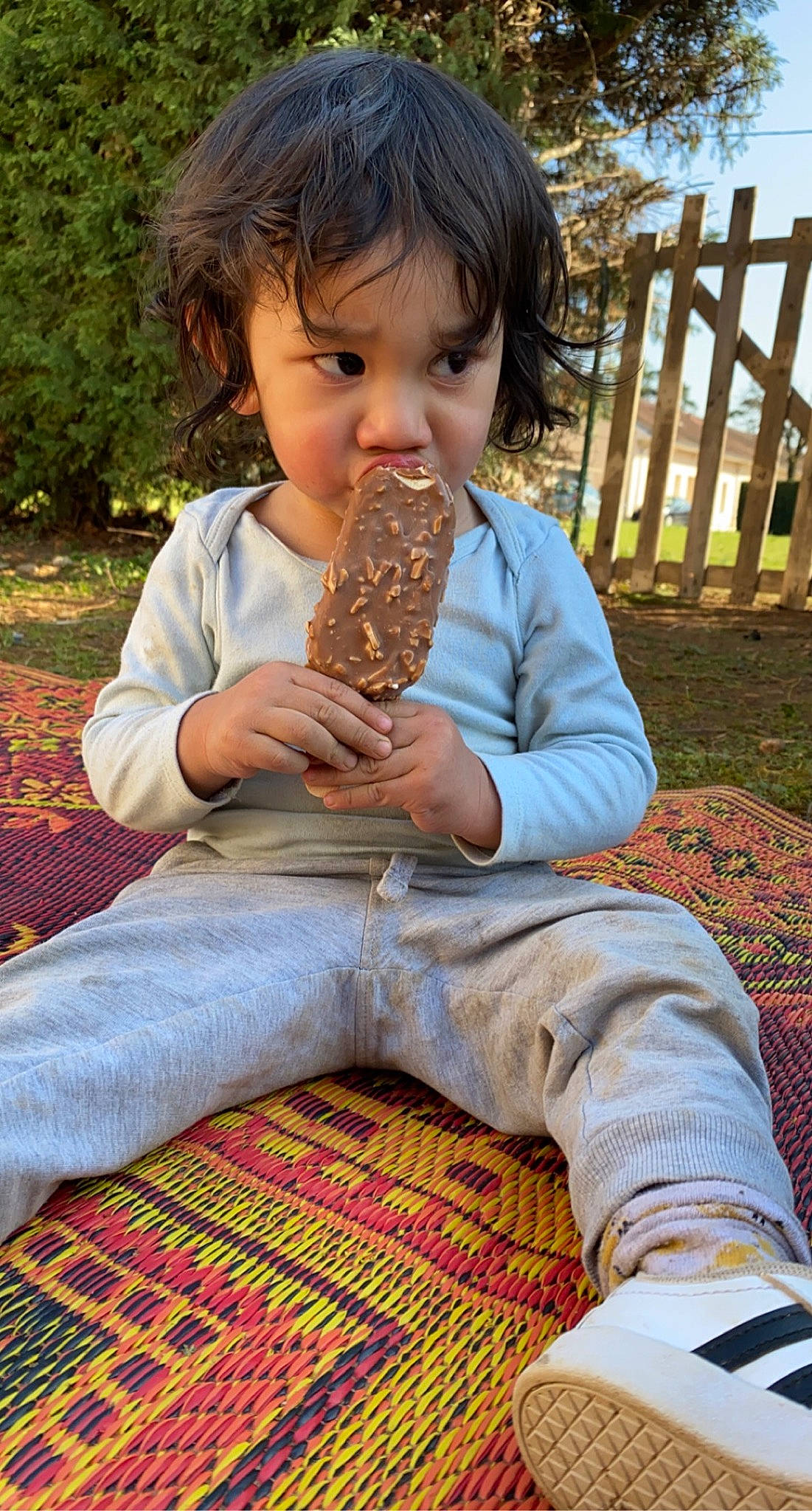 Nolann participe au concours pour gagner de l'argent avec cette photo : baby_toddler_clothing, blue, child, fence, flooring, fun, grass, green, happy, leaf, leisure, pattern, people_in_nature, person, photograph, sitting, sky, thumb, toddler, wood
