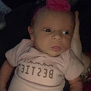 Ayla joined the competition — help win amazing prizes! baby, newborn, infant, pink_headband, flower, shirt, text_on_clothing, hand, adult_hand, dark_background, dim_lighting, portrait, child, cute, sleepy, lying_down, person, clothing, closeup, indoors