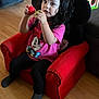 balls, black_pants, child, couch, curious, cute, furniture, girl, indoor, living_room, minnie_mouse, person, pigtails, pink_shirt, playful, red_chair, socks, toddler, toy, wooden_floor