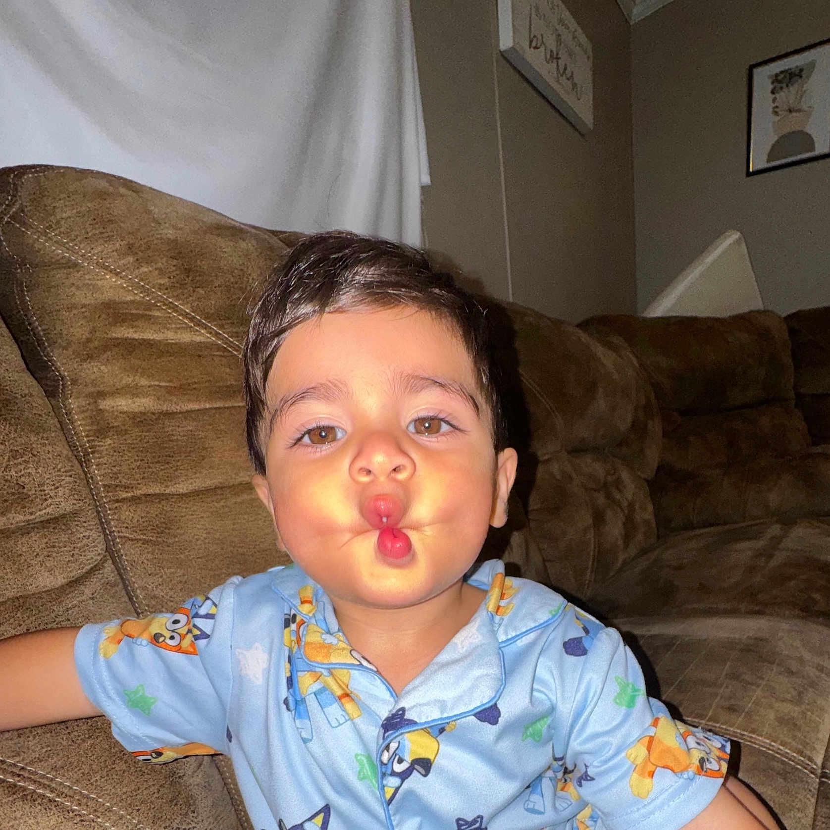 Isaias joined the competition — help win amazing prizes! child, toddler, baby, portrait, face, smiling, puckering, kissy_face, sitting, couch, sofa, pajamas, cartoon_clothing, blue_clothing, indoor, living_room, furniture, flash_photography, brown_couch, home