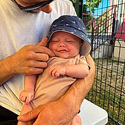 Tymëlio a rejoint le concours — aidez-le/la à gagner de superbes lots ! baby, man, hat, outdoor, smile, sunglasses, hand, fence, table, grass, shirt, person, holding, infant, skin, arm, face, daylight, expression, casual
