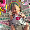baby, infant, baby_seat, rainbow, toy, mittens, sunlight, indoor, colorful, happy, child, cute, patterned_fabric, playtime, closeup, smiling_sun, hanging_toy, pink, yellow, purple