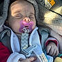 baby, sleeping, pacifier, blanket, car_seat, child, infant, toy, clothing, hand, safety_harness, closeup, indoors, face, cute, peaceful, warm, soft_light, car_interior, accessory