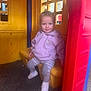 toddler, child, playhouse, plastic, purple_hoodie, striped_pants, white_shoes, indoor_play_area, smiling, seated, colorful, yellow_wall, red_frame, window, playground, young_child, casual_clothing, happy, cute, small