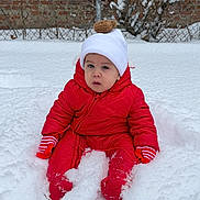 Eithan is registered to the contest to win money with this photo: toddler, child, snow, winter, red_snowsuit, mittens, hat, pom_pom, outdoor, cold_weather, snowy_ground, fence, bare_branches, winter_clothing, sitting, young_child, face, expression, nature, daytime