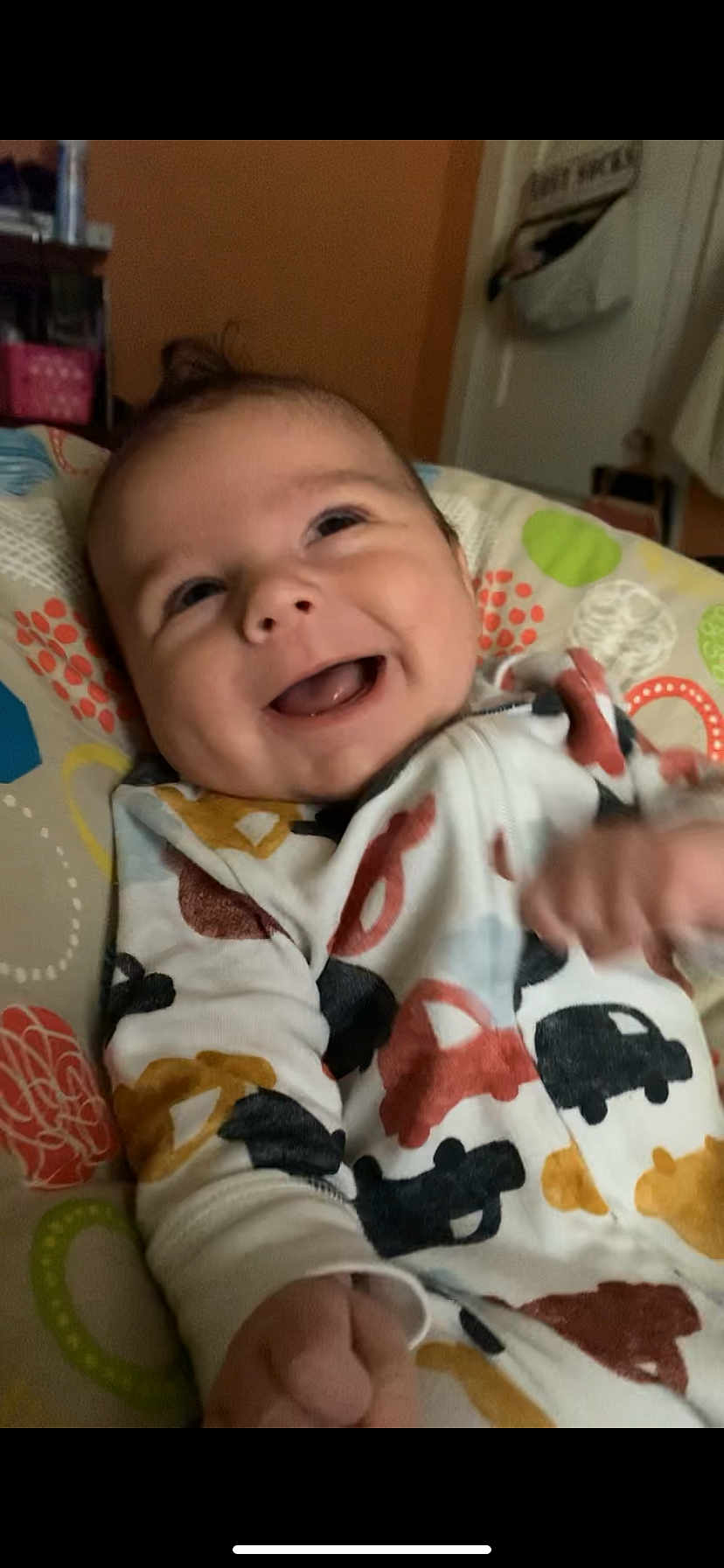Easton is registered to the contest to win money with this photo: baby, smiling, infant, cute, happy, patterned_clothing, car_print, cushion, colorful, indoor, child, face, portrait, young, lying_down, expression, hand, cozy, playful, soft