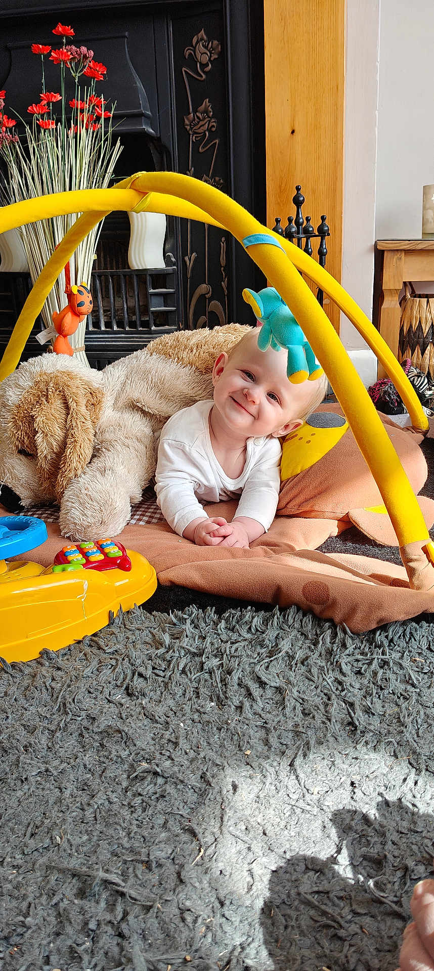 Lyla joined the competition — help win amazing prizes! baby, child, smile, play_mat, toy, stuffed_animal, floor, carpet, indoor, colorful, yellow, orange, blue, white_clothing, face, hand, head, cute, happy, playtime