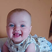 Margot participe au concours pour gagner de l'argent avec cette photo : baby, smiling, blue_eyes, floral_dress, infant, happy, cute, child, portrait, indoors, soft_lighting, skin, face, person, toddler, lying_down, white_surface, warm_background, cheerful, closeup
