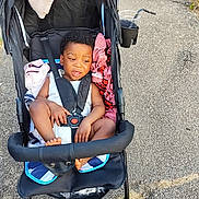 Kris-Emmanuel participe au concours pour gagner de l'argent avec cette photo : baby_clothes, blanket, casual, child, cup_holder, curly_hair, expression, footwear_free, grass, outdoor, pavement, plastic_cup, seatbelt, sidewalk, stroller, summer, sunlight, toddler, towel, wheels