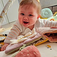 Rose participe au concours pour gagner de l'argent avec cette photo : baby, infant, smile, face, eyes, cheeks, hair, hand, play_mat, hanging_toys, plush_toy, strawberry_toy, soft_book, onesie, crawling, nursery, wooden_floor, door, blanket, indoor