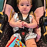 Lilith joined the competition — help win amazing prizes! baby, car_seat, child, infant, toy, book, pink, black, clothing, hair, hands, face, seat_belt, portrait, indoor, expression, cute, young_child, sitting, playful