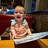 baby, child, high_chair, menu, restaurant, smile, happy, girl, people, indoor, table, clothing, hair, glasses, adult, conversation, booth, lighting, window, wood