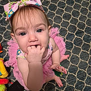 Lilith is registered to the contest to win money with this photo: baby, child, girl, pink_bow, tutu, hand_in_mouth, carpet, patterned_rug, toys, curious, blue_eyes, sitting, indoor, cute, infant, clothing, headwear, fingers, looking_up, person