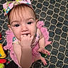 baby, child, girl, pink_bow, tutu, hand_in_mouth, carpet, patterned_rug, toys, curious, blue_eyes, sitting, indoor, cute, infant, clothing, headwear, fingers, looking_up, person